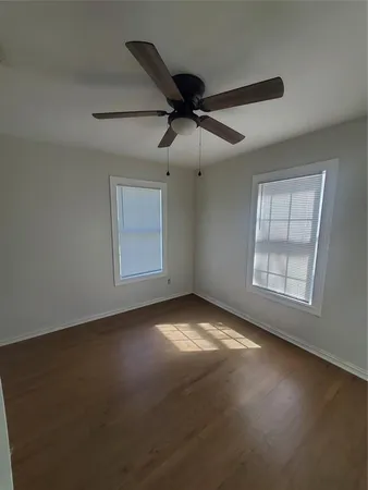 an empty room with wooden floor fan and windows
