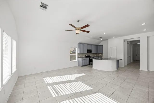 a living room with kitchen view and a ceiling fan with a rug