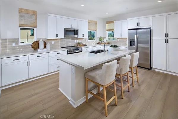 a kitchen with stainless steel appliances granite countertop a stove a refrigerator a microwave a sink and white cabinets with wooden floor