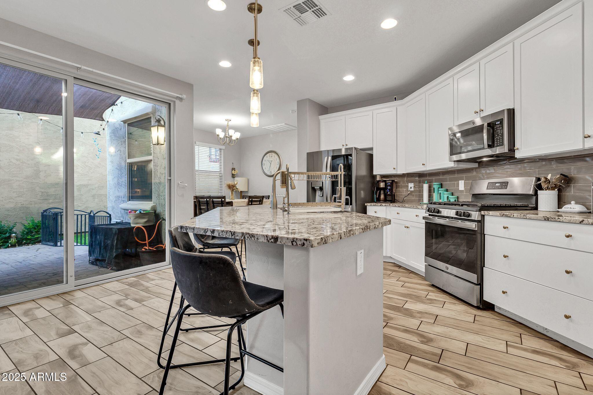 4145 East Bethena Street Gilbert, AZ 85295 - Photo 11 of 60 a kitchen with stainless steel appliances kitchen island granite countertop a stove a sink a refrigerator and white cabinets with wooden floor