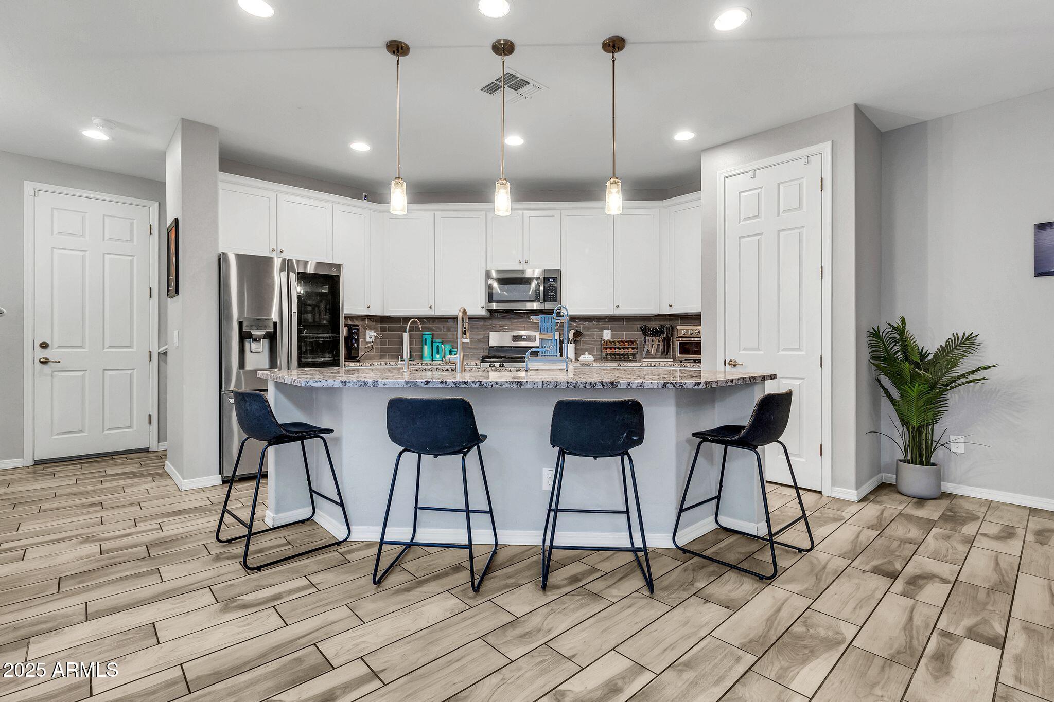 4145 East Bethena Street Gilbert, AZ 85295 - Photo 12 of 60 a kitchen with stainless steel appliances kitchen island granite countertop a dining table chairs and white cabinets