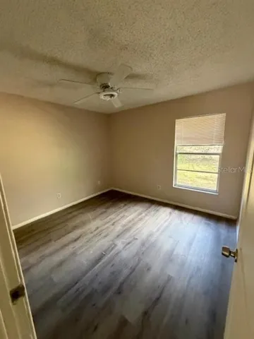 an empty room with wooden floor fan and window