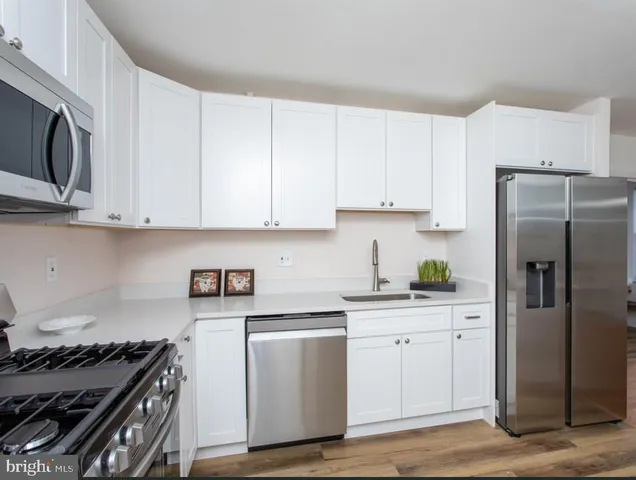 a kitchen with stainless steel appliances granite countertop a stove a refrigerator a sink dishwasher and white cabinets with wooden floor