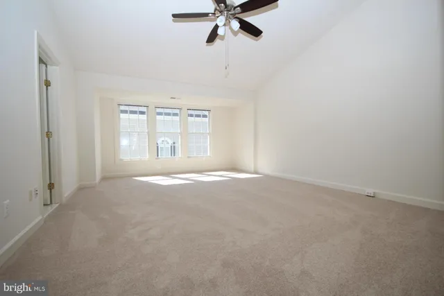 an empty room with chandelier fan and windows