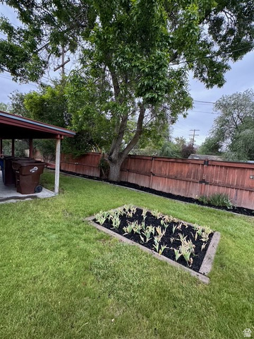 189 West Center Street Midvale, UT 84047 - Photo 47 of 64 Expansive backyard featuring a lush lawn, a mature shade tree, a raised garden bed with planted greenery, and a wood fence enclosing the perimeter