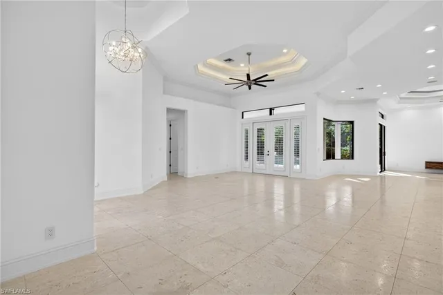 a view of an empty room with chandelier fan and kitchen view