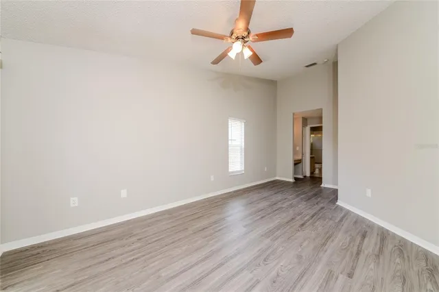 an empty room with wooden floor chandelier fan and windows