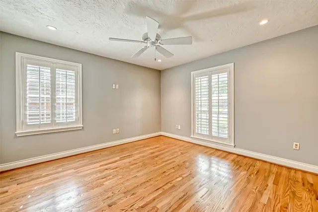 an empty room with wooden floor fan and windows