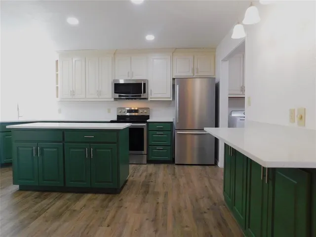 a kitchen with kitchen island granite countertop wooden floors stainless steel appliances and sink