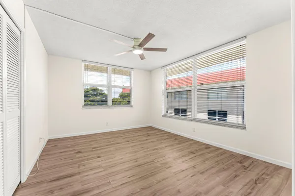 an empty room with wooden floor fan and windows