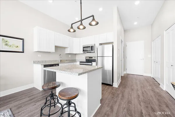 a kitchen with granite countertop a refrigerator a stove a sink and white cabinets with wooden floor