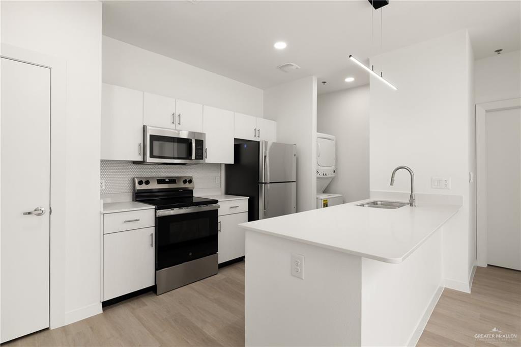 412 South Ware Road McAllen, TX 78501 - Photo 5 of 7 Kitchen with light hardwood / wood-style flooring, stainless steel appliances, sink, decorative backsplash, and stacked washer / dryer