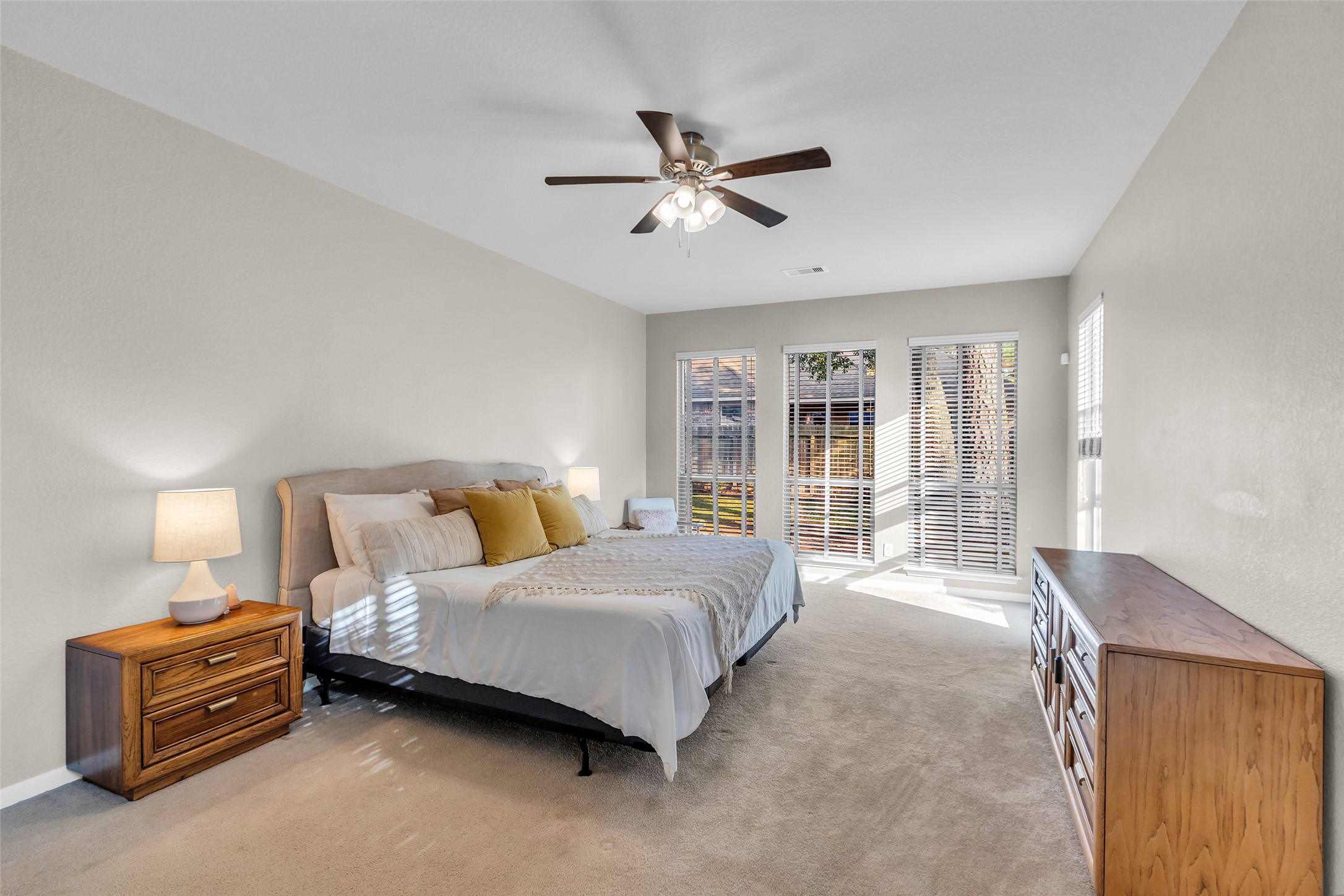155 Magnolia Grove Lane Conroe, TX 77384 - Photo 11 of 25 Primary bedroom with natural light streams through expansive windows with blinds, highlighting the neutral carpet and walls. A ceiling fan adds comfort and style.