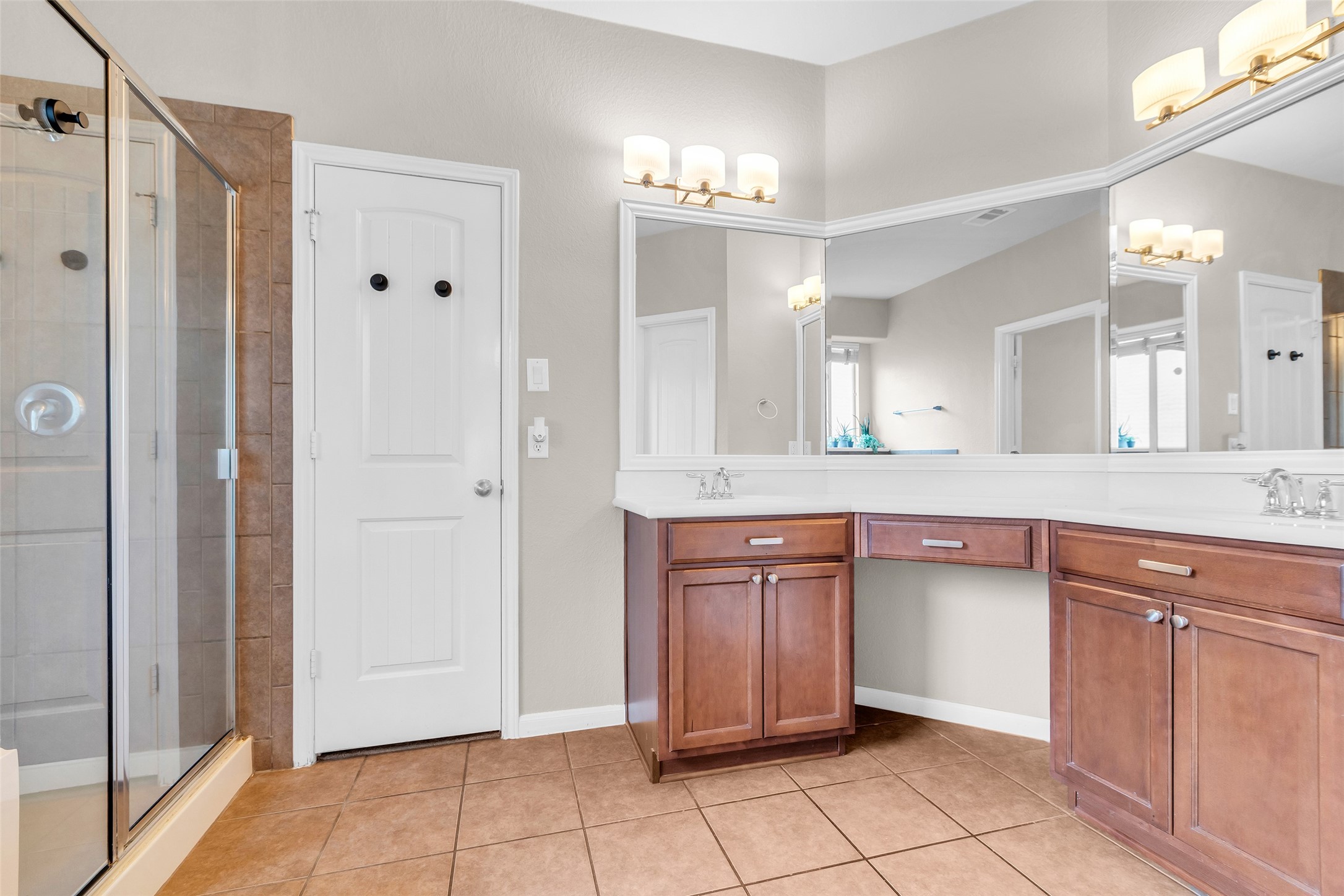 155 Magnolia Grove Lane Conroe, TX 77384 - Photo 13 of 25 Spacious shower with glass doors, dual vanities with ample storage, large mirrors, and bright lighting. The warm wood cabinetry and neutral tile flooring create a welcoming ambiance.