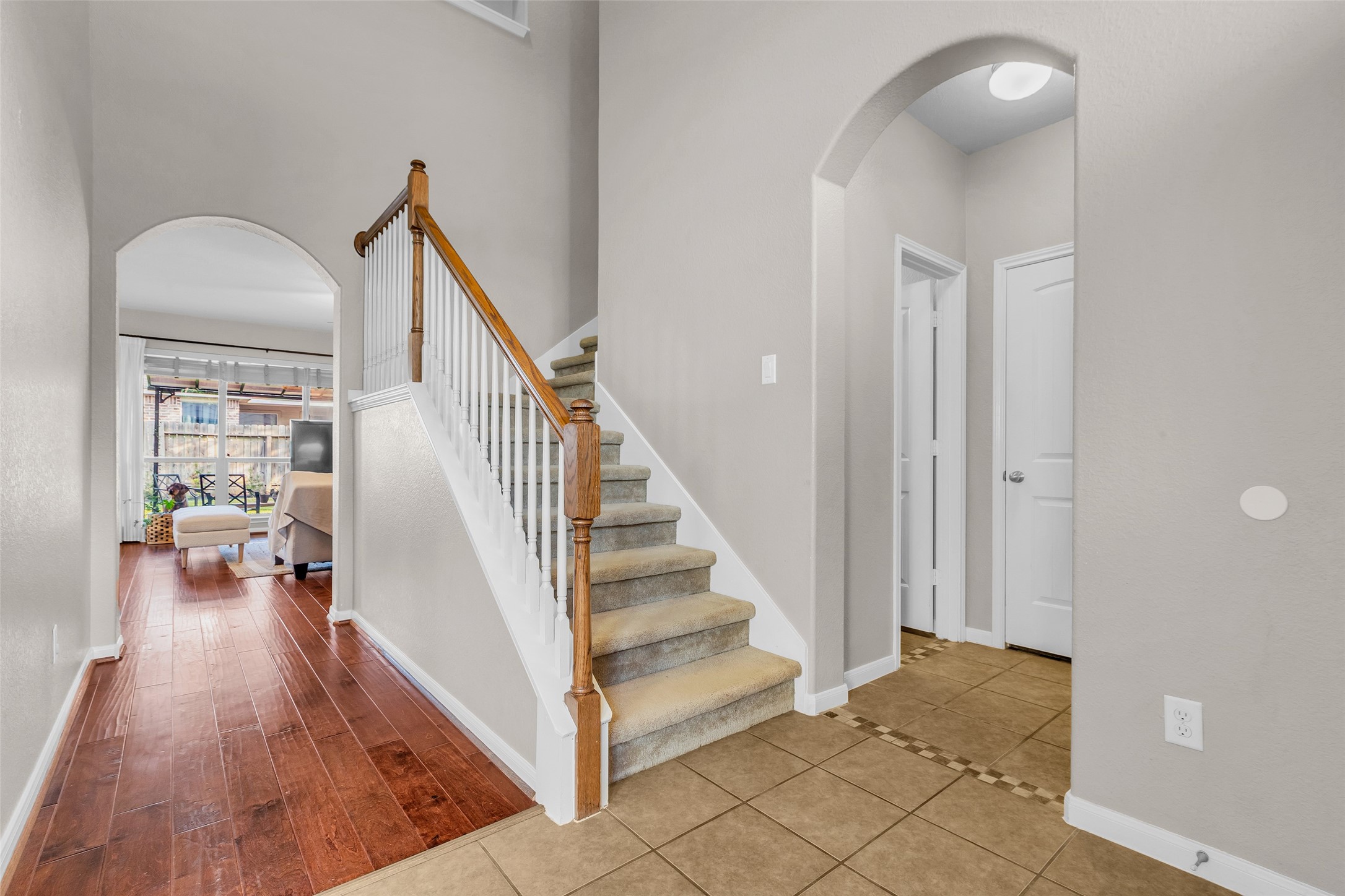 155 Magnolia Grove Lane Conroe, TX 77384 - Photo 15 of 25 entryway with tiled flooring leading to carpeted stairs and a hallway. Arched doorways open to a cozy living area featuring hardwood floors and a large window.
