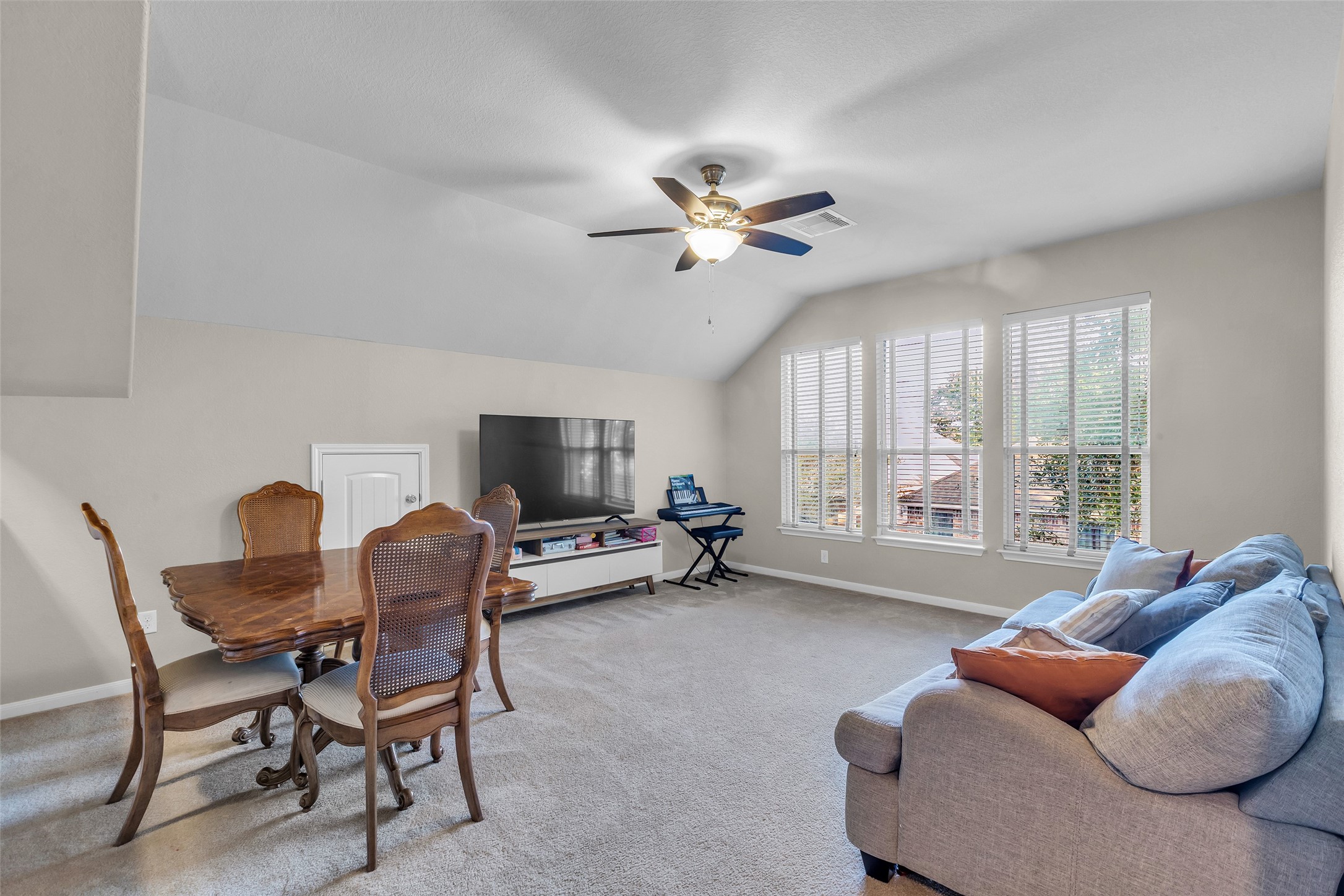 155 Magnolia Grove Lane Conroe, TX 77384 - Photo 16 of 25 Gameroom features a vaulted ceiling with a ceiling fan, large windows for natural light with neutral carpet flooring, creating a warm and inviting atmosphere.