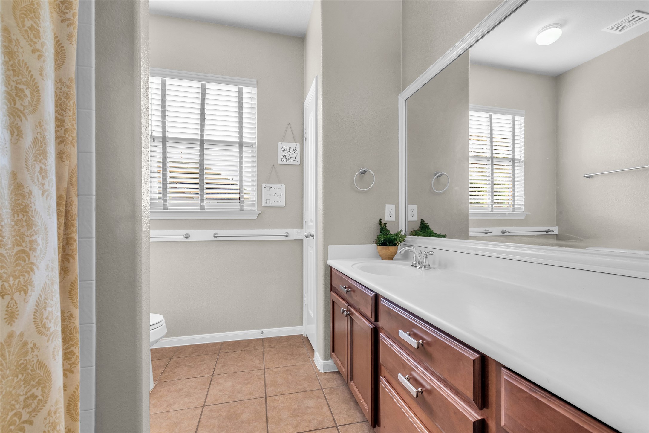 155 Magnolia Grove Lane Conroe, TX 77384 - Photo 18 of 25 This bathroom features a spacious countertop with a large mirror, wooden cabinetry, and a neutral color palette. It has tiled flooring, a window for natural light.