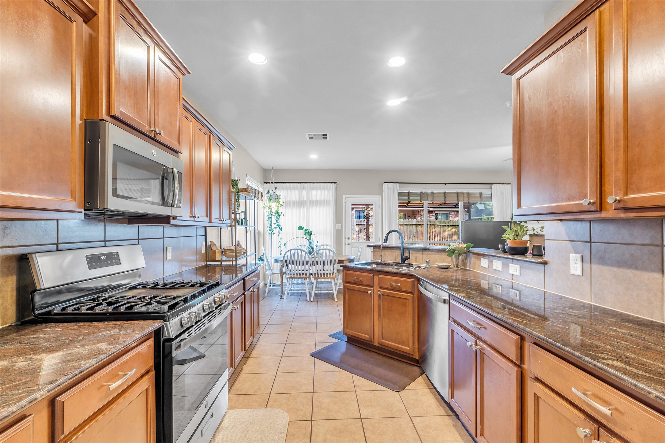 155 Magnolia Grove Lane Conroe, TX 77384 - Photo 8 of 25 Wooden cabinetry, stainless steel appliances, and a spacious layout with a central island. It opens to a bright dining area with large windows, providing ample natural light and a view of the backyard.