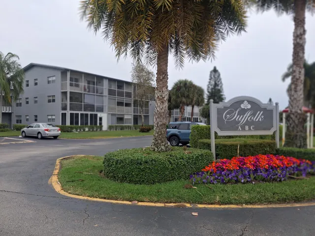 a sign board with a building and garden in the background