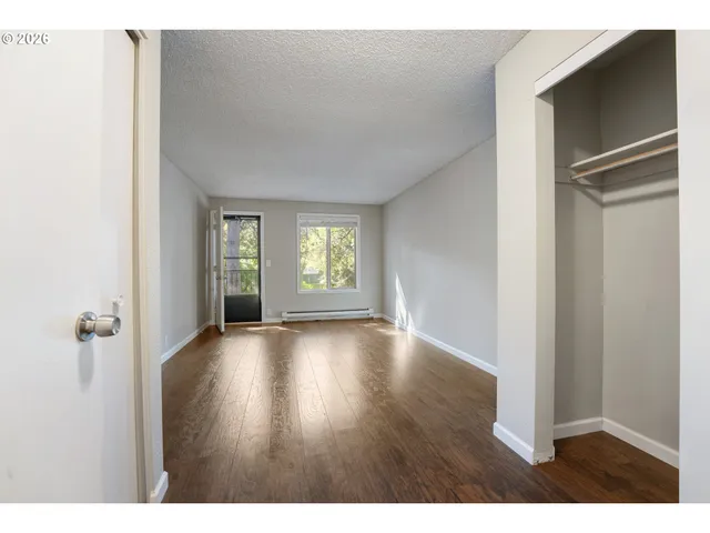 a view of an empty room with window and wooden floor
