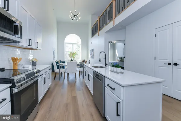 a large kitchen with stainless steel appliances a stove a sink dishwasher and white cabinets with wooden floor