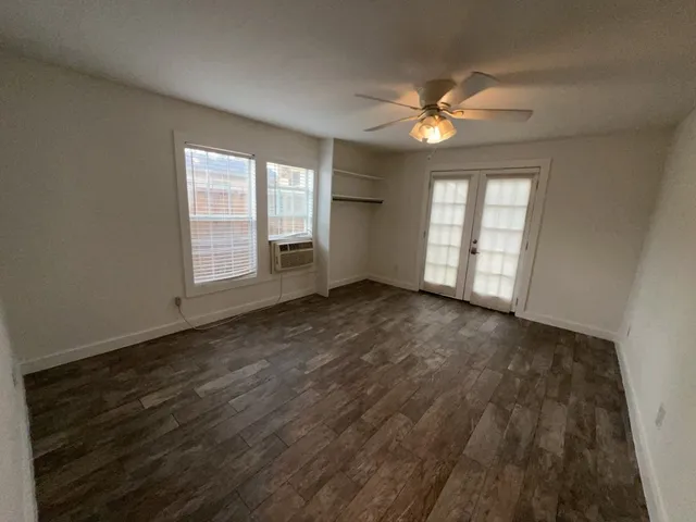 an empty room with wooden floor fan and windows