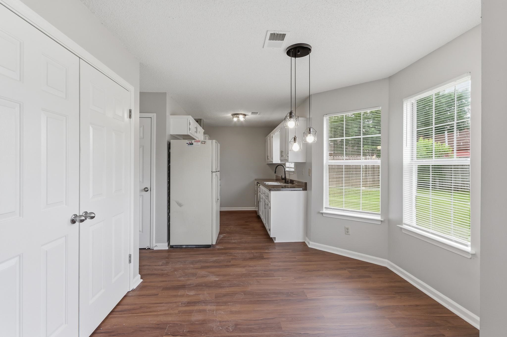 4101 Long Creek Road Memphis, TN 38125 - Photo 15 of 36 Open concept kitchen and dining area featuring wood-finish flooring, white cabinetry, a modern pendant light fixture, and multiple windows