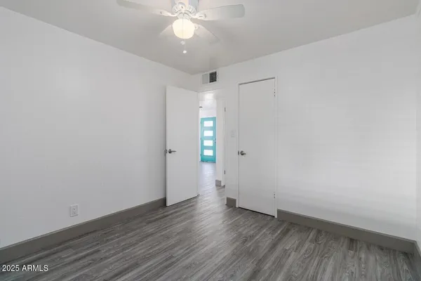 a view of an empty room with wooden floor and a ceiling fan
