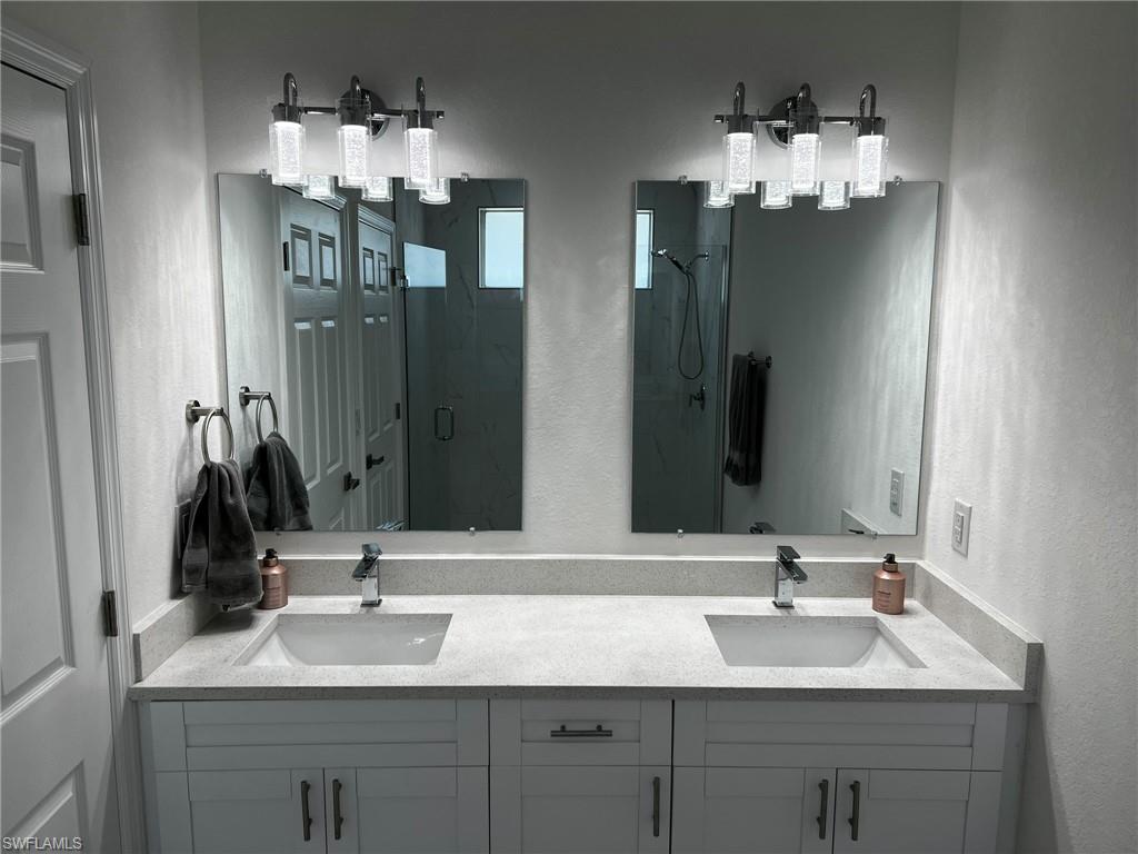 3313 68th Street West Lehigh Acres, FL 33971 - Photo 21 of 26 Full bath featuring double vanity, a shower stall, a textured wall, and a sink