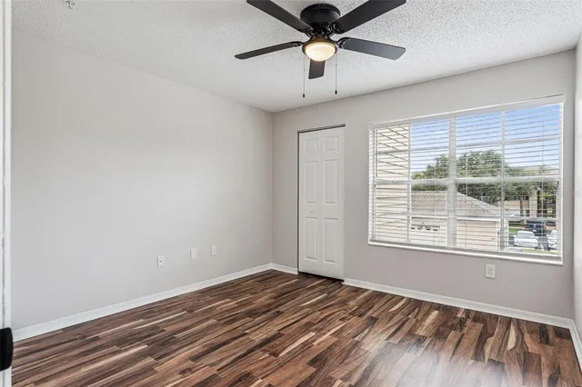 an empty room with wooden floor chandelier fan and windows