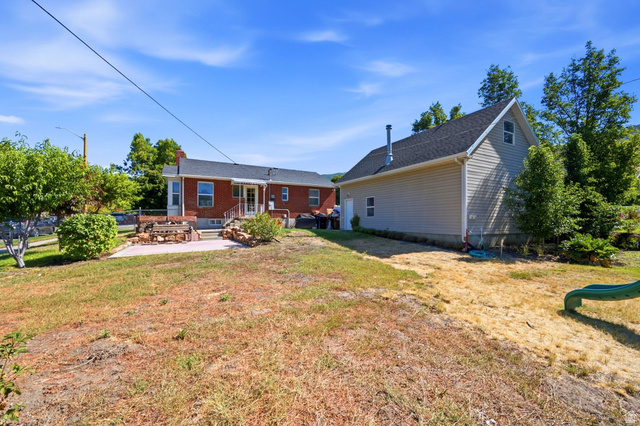 310 East 600 South Centerville, UT 84014 - Photo 28 of 41 Expansive backyard featuring a brick exterior home with a patio, a separate detached structure with siding, and mature trees