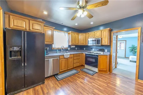 a kitchen with stainless steel appliances granite countertop a refrigerator a sink dishwasher a stove and white countertops with wooden floor