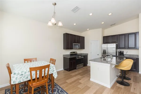 a kitchen with stainless steel appliances granite countertop a stove a refrigerator a kitchen island a sink dishwasher a dining table and chairs with wooden floor