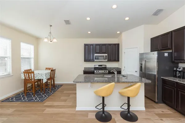 a kitchen with stainless steel appliances kitchen island granite countertop a table chairs sink refrigerator and microwave