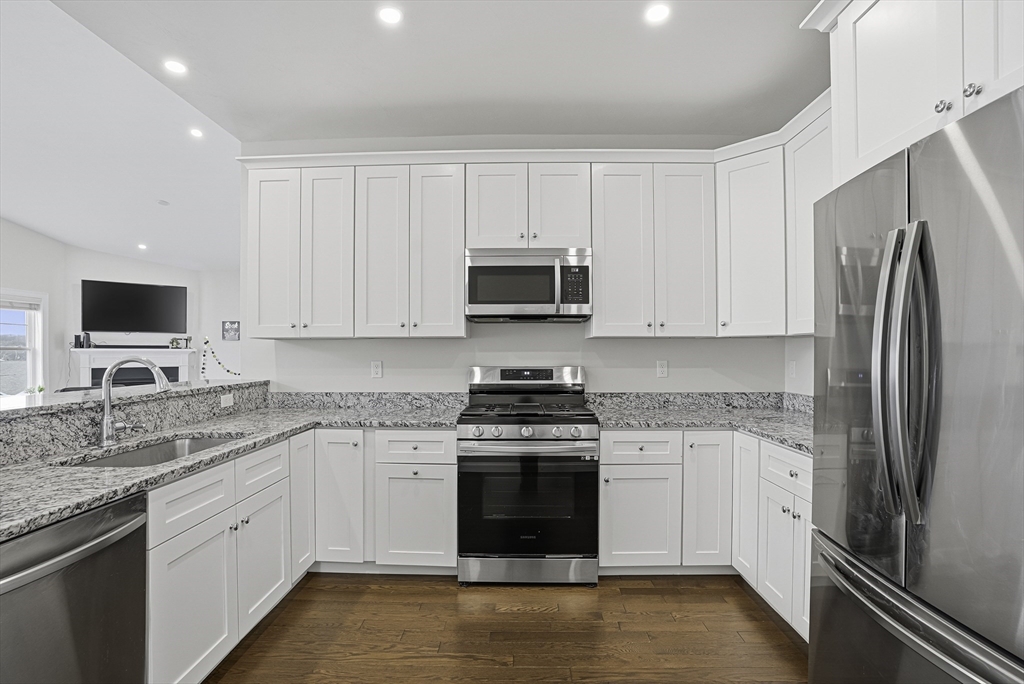 52 Logans Run, Unit 52 Millbury, MA 01527 - Photo 4 of 41 a kitchen with stainless steel appliances granite countertop a stove top oven a refrigerator and a sink with wooden floor