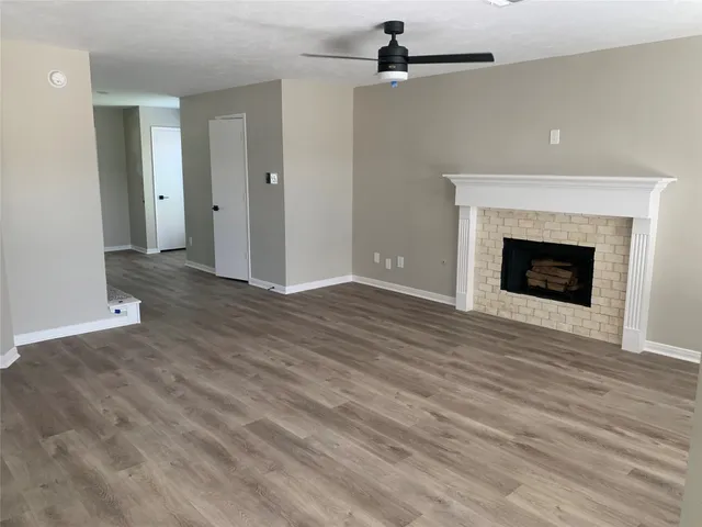 a view of an empty room with wooden floor fireplace and a window