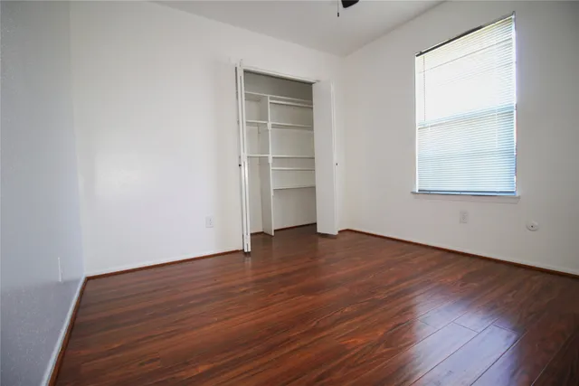 an empty room with wooden floor closet and windows