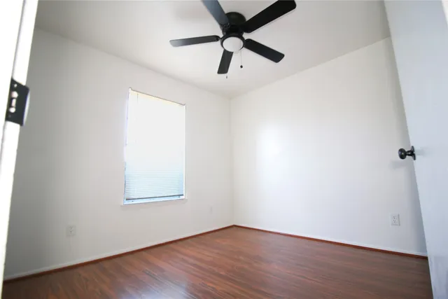 an empty room with wooden floor chandelier fan and windows