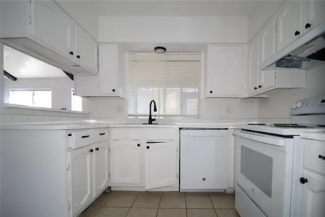 a kitchen with white cabinets appliances a sink and a window