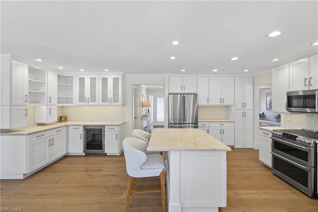 4916 Crayton Road Naples, FL 34103 - Photo 14 of 34 a large kitchen with kitchen island granite countertop a stove a sink a refrigerator and white cabinets with wooden floor