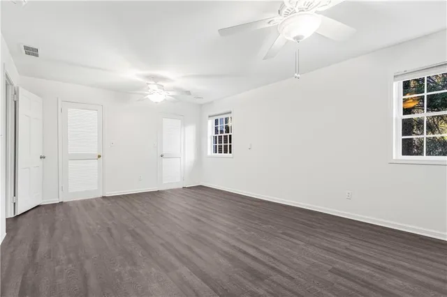 an empty room with wooden floor chandelier fan and windows