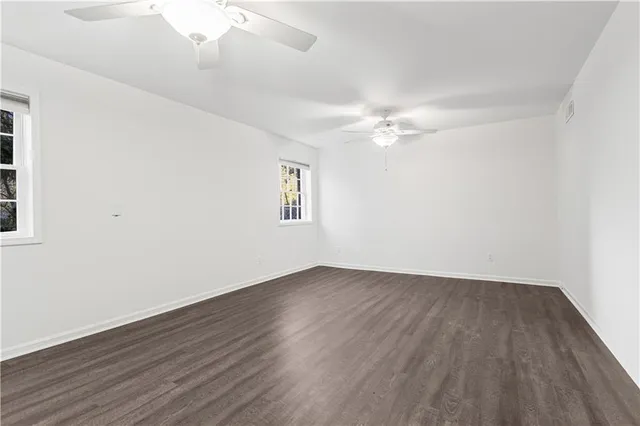 an empty room with wooden floor fan and windows