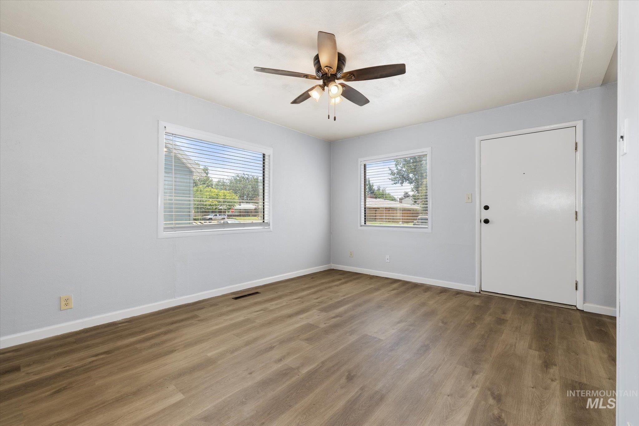 918 West 3rd Street Weiser, ID 83672 - Photo 7 of 36 Bright interior space featuring wood-finish flooring, two large windows with blinds, a ceiling fan with integrated lighting, and a white entry door