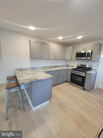 a kitchen with kitchen island granite countertop a stove top oven a sink dishwasher and a refrigerator with wooden floor