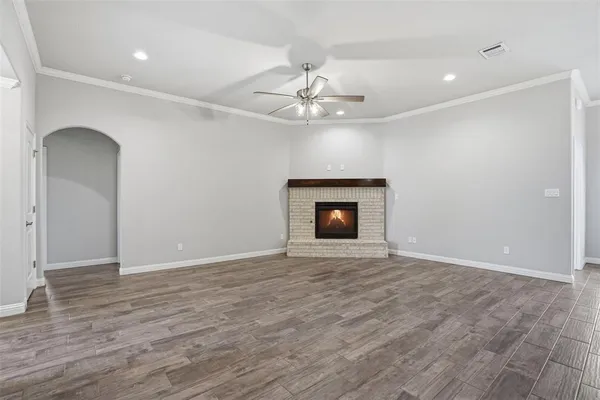 an empty room with wooden floor a ceiling fan a fireplace and windows