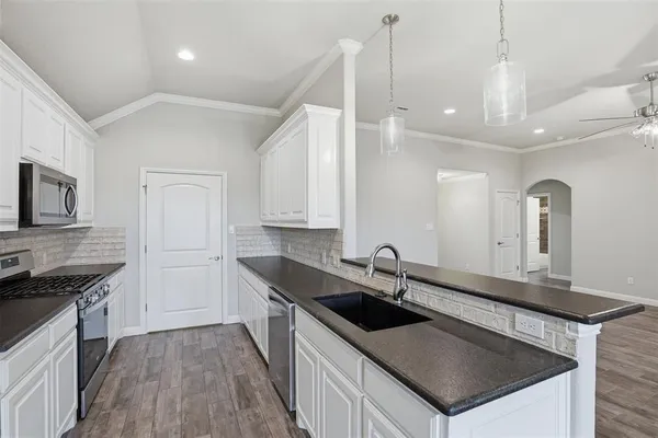 a kitchen that has a sink a microwave oven a stove and white cabinets with wooden floor