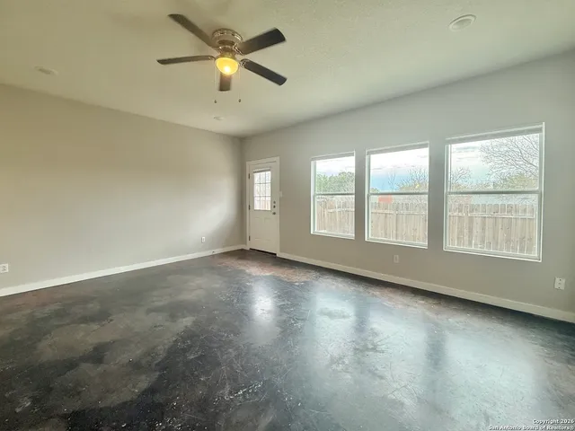 an empty room with chandelier fan and windows
