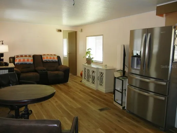 a living room with stainless steel appliances furniture a refrigerator and a dining table