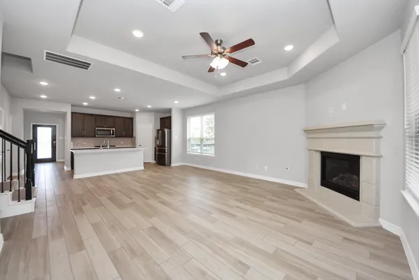 an empty room with wooden floor a ceiling fan and kitchen view