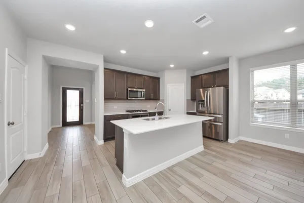 a kitchen with stainless steel appliances a stove top oven a sink dishwasher a refrigerator and a dining table with wooden floor